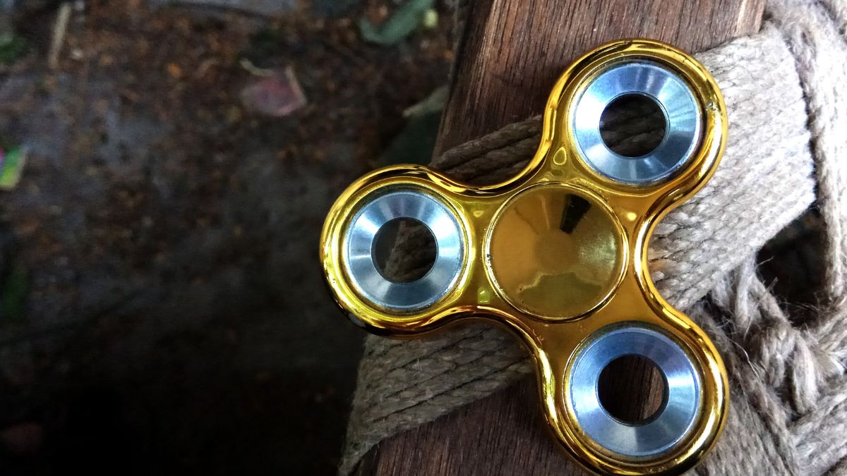 Ein goldfarbener Fidget Spinner liegt auf einem Holzuntergrund.