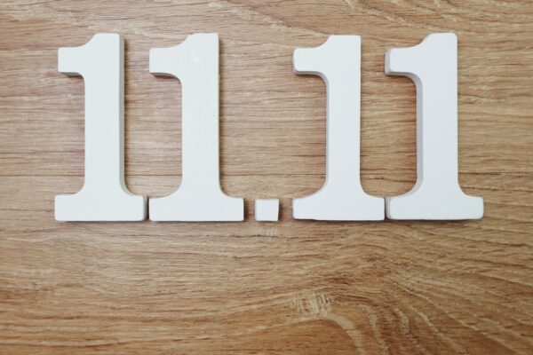 Die Zahlen 11.11 aus weißen Holzbuchstaben auf einem Holztisch.
