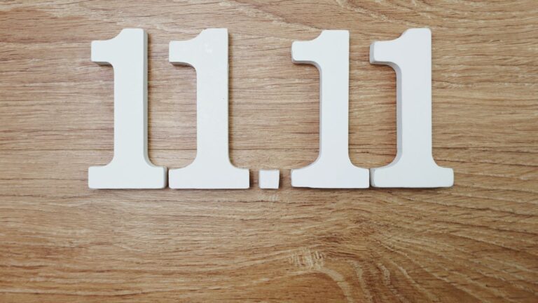 Die Zahlen 11.11 aus weißen Holzbuchstaben auf einem Holztisch.