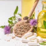 Eine Holzschaufel mit Mariendistel-Pulver, umgeben von Pflanzen und Ölen.