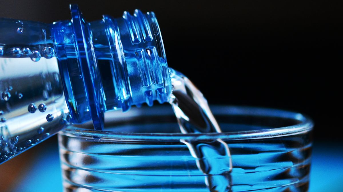 Eine Flasche mit Wasser, die in ein Glas gegossen wird, zeigt frisches, sprudelndes Wasser.