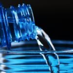 Eine Flasche Wasser, die in ein Glas gegossen wird, symbolisiert Gesundheit.
