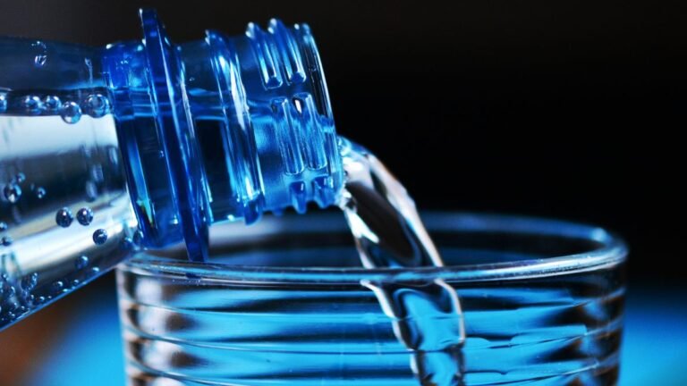 Eine Flasche Wasser, die in ein Glas gegossen wird, symbolisiert Gesundheit.