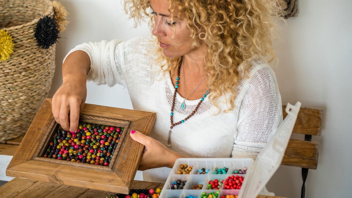 Eine Frau sortiert bunte Perlen in einen Holzrahmen, während sie konzentriert arbeitet.