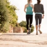 Zwei Frauen gehen auf einem Weg, umgeben von Natur, was die Vorteile des Gehens symbolisiert.