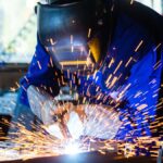 Ein Schweißer arbeitet präzise mit einem Impulsschweißgerät, Funken sprühen.