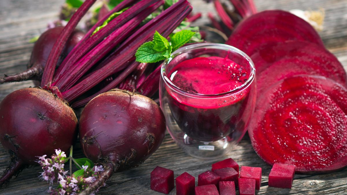 Frische Rote Bete mit Saft und geschnittenen Scheiben auf Holzuntergrund.