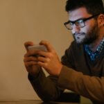Blaues Licht: wie es unser Wohlbefinden im Alltag beeinflusst Ein Mann schaut konzentriert auf sein Smartphone, während er in einem dunklen Raum sitzt.