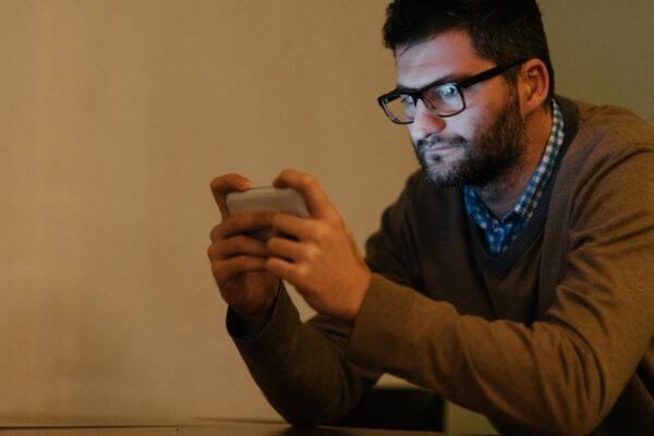 Ein Mann schaut konzentriert auf sein Smartphone, während er in einem dunklen Raum sitzt.