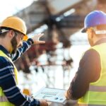 Zwei Bauarbeiter besprechen Pläne auf einer Baustelle mit Entlastungsringen.