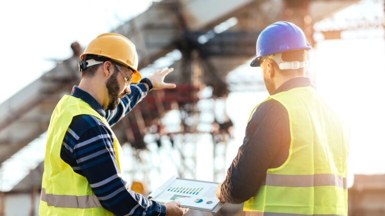 Zwei Bauarbeiter besprechen Pläne auf einer Baustelle mit Entlastungsringen.