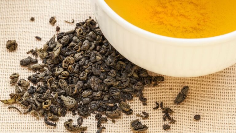 Eine Tasse Gunpowder-Tee mit losem, gerolltem Grüntee daneben.