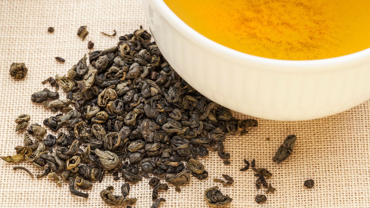 Eine Tasse Gunpowder-Tee mit losem, gerolltem Grüntee daneben.