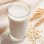 Ein Glas Hafermilch steht auf einem Tisch, umgeben von Haferkörnern.