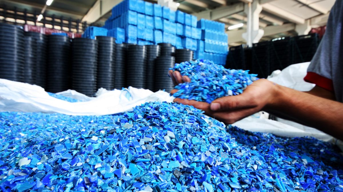Hände halten blaue Kunststoffreste über einem Haufen in einer Fabrik.