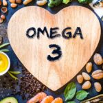 Eine Holzplatte in Herzform mit der Aufschrift Omega 3, umgeben von gesunden Lebensmitteln.