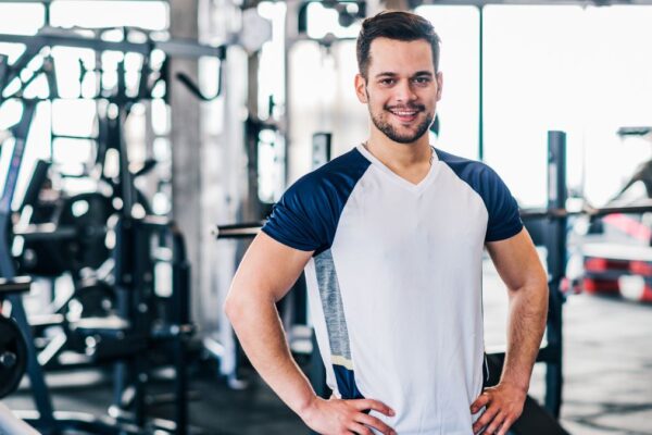 Ein sportlicher Mann in einem Fitnessstudio, der lächelt und Selbstbewusstsein ausstrahlt.