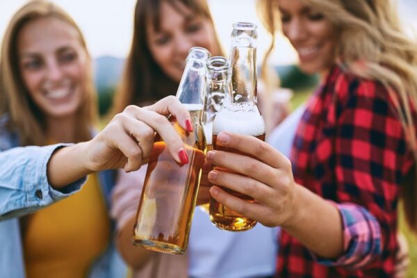 Drei junge Frauen stoßen mit Bierflaschen an einem sonnigen Tag an.