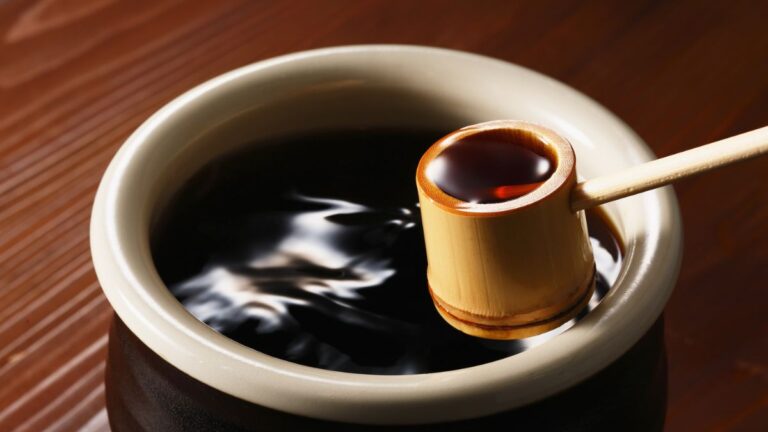 Eine Schale mit Sojasauce und einem Bambuslöffel, der die dunkle Flüssigkeit hält.