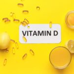 Ein gelbes Bild mit Vitamin D Kapseln, einer Zitrone und einem Glas Saft.