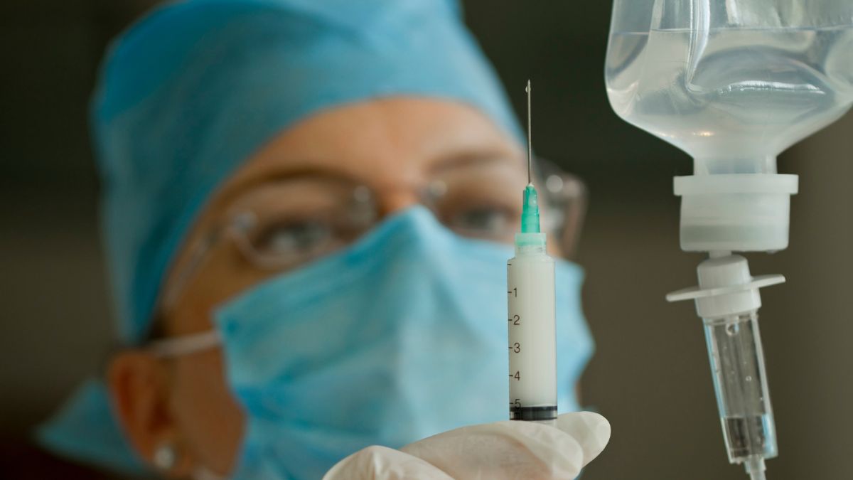 Eine Krankenschwester hält eine Spritze und einen Tropf in der Hand.